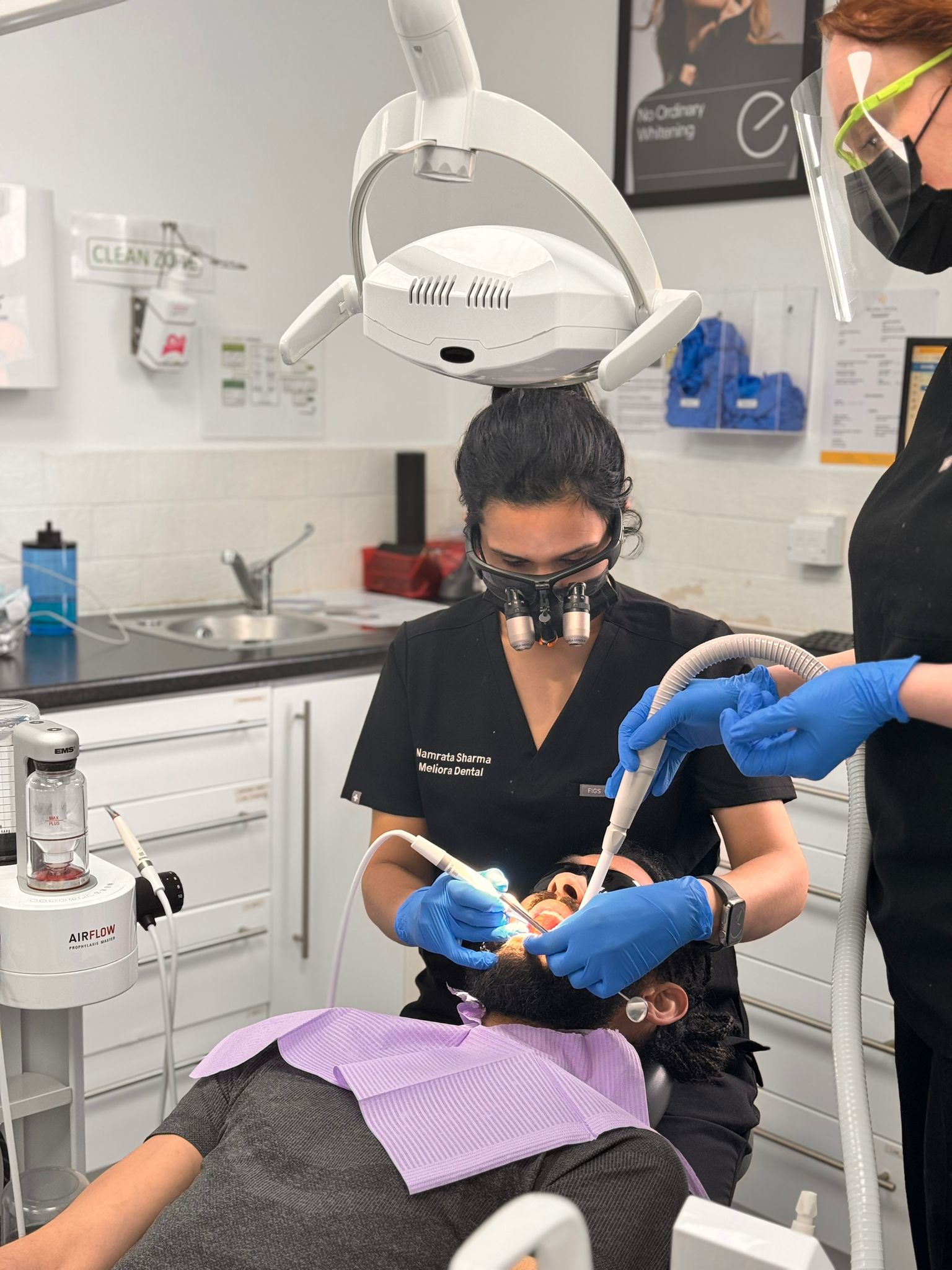 Dr Namrata is a dental hygienist Leeds. is performing a scale and polish for a patient. Her dental nurse is stood next to her administering water into the patient's mouth. 